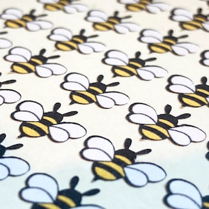 May include: A sheet of white paper with a repeating pattern of black and yellow bees with white wings. The bees are arranged in rows.
