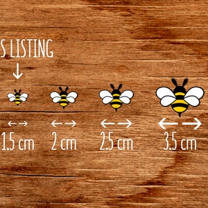 May include: Four bee illustrations on a wood background. The bees are black and yellow with white wings. The bees are shown in different sizes with measurements in centimeters: 1.5 cm, 2 cm, 2.5 cm, and 3.5 cm.