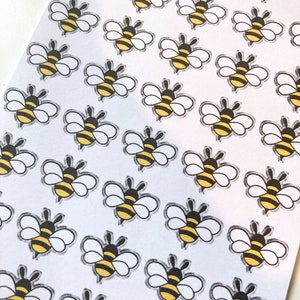 May include: A sheet of white paper with multiple black and yellow bee stickers. The bees have black eyes, black legs, and white wings.