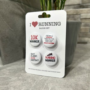May include: A set of three white round badges with red and black text. The badges feature running-themed slogans, including "10K Wanker", "I'm not a jogger. They're the ones that find the dead bodies", "Eat. Sleep. Run. Repeat." and "Running Wanker".