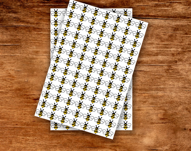 May include: Two sheets of white paper with a repeating pattern of yellow and black cartoon bees.