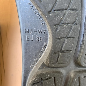 May include: Close-up of the sole of a black shoe. The sole has a textured pattern and the text "PATENTED", "M5-W7", "EU 38", and "Made in Korea" are visible.