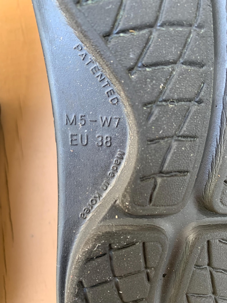 May include: Close-up of the sole of a black shoe. The sole has a textured pattern and the text "PATENTED", "M5-W7", "EU 38", and "Made in Korea" are visible.
