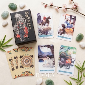 May include: A tarot card deck with a black box featuring a warrior and horse illustration. The deck includes several cards with watercolor-style artwork depicting figures and scenes. Decorative stones and flowers surround the deck.