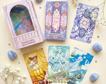 Può includere: Un mazzo di carte dei tarocchi con una scatola rosa e viola con un'illustrazione di un castello. Vengono mostrate diverse carte dei tarocchi, che mostrano opere d'arte colorate con figure e disegni floreali. Pietre blu e fiori bianchi sono sparsi.