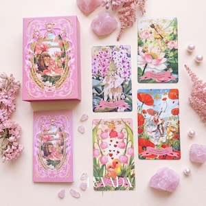 May include: A pink tarot deck box and guidebook set titled Blooming Booming Mint & Oats, accompanied by four illustrated tarot cards featuring fantasy scenes with animals, flowers, and fairies, surrounded by pink crystals and floral sprigs.