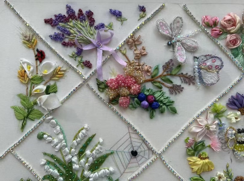 K&ouml;nnte beinhalten: Eine wei&szlig;e dekorative Tafel mit gestickten Blumendesigns. Die Tafel zeigt Lavendel, Rosen, Calla-Lilien und andere Blumen sowie eine Libelle, einen Schmetterling und ein Spinnennetz. Die Gitterlinien sind mit funkelnden Strasssteinen akzentuiert.