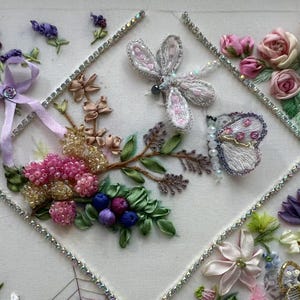 K&ouml;nnte beinhalten: Gestickte Blumenkunst mit einem Lavendelstrau&szlig; mit lila Band, rosa Rosen, einer Libelle und einem Schmetterling. Das Kunstwerk enth&auml;lt Perlenakzente und ist mit Strasssteinen eingefasst.