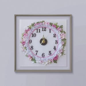 May include: A framed clock with a white face and black numbers. The clock is decorated with pink and white ribbon flowers.