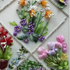 K&ouml;nnte beinhalten: Detaillierte Blumen-Bandstickerei mit verschiedenen Blumen in Wei&szlig;, Orange, Lila, Rosa und Blau. Die Blumen sind in einem Rautenmuster angeordnet, das mit glitzernden Strasssteinen umrandet ist. Gr&uuml;ne Bl&auml;tter und Stiele erg&auml;nzen das Design.