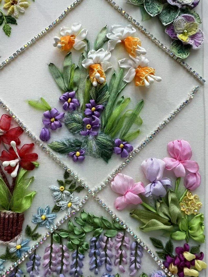 K&ouml;nnte beinhalten: Detaillierte Blumen-Bandstickerei mit verschiedenen Blumen in Wei&szlig;, Orange, Lila, Rosa und Blau. Die Blumen sind in einem Rautenmuster angeordnet, das mit glitzernden Strasssteinen umrandet ist. Gr&uuml;ne Bl&auml;tter und Stiele erg&auml;nzen das Design.