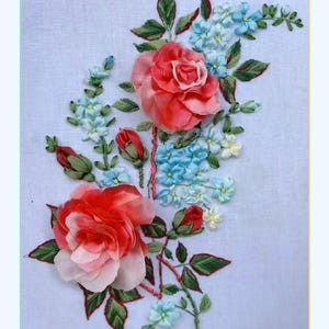 May include: A close-up of a hand-stitched embroidery design featuring pink and red roses and blue forget-me-nots on a white linen fabric.