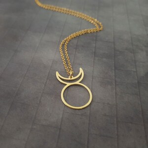 Op de afbeelding: Een gouden ketting met een hanger in de vorm van een cirkel met een halve maan aan elke kant.