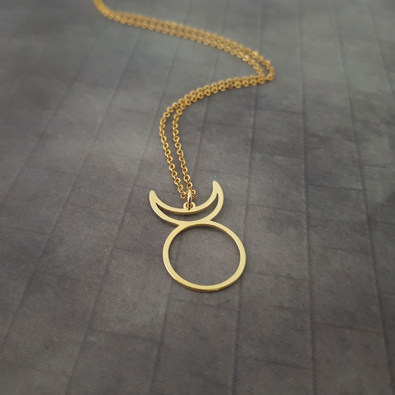 Op de afbeelding: Een gouden ketting met een hanger in de vorm van een cirkel met een halve maan aan elke kant.