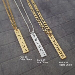 May include: Three vertical bar necklaces with custom engravings. The first is a gold cable chain with "MRIANA" in Font #7. The second is a silver box chain with "AURORA" in Font #8. The third is a gold figaro chain with "ADDISON" in Font #32.