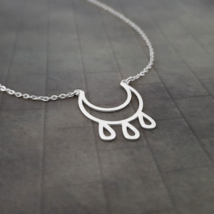 May include: A silver necklace with a crescent moon pendant and four teardrop-shaped charms hanging from the bottom.
