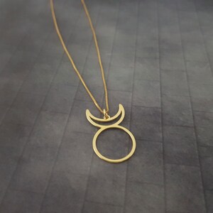 Op de afbeelding: Een gouden ketting met een hanger met een cirkel met twee halve manen erop. De hanger is een eenvoudig, minimalistisch ontwerp.