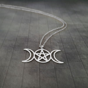 May include: A silver necklace with a triple moon and pentacle pendant. The pendant is a symbol of the three phases of the moon and the five elements.