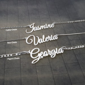 May include: Three silver necklaces with different chain styles: cable, box, and figaro. Each necklace features a personalised nameplate with the names "Jasmine", "Valeria", and "Georgia" in a cursive script.