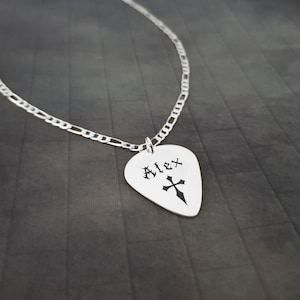 May include: Silver guitar pick necklace with the name "Alex" and a cross engraved on it.