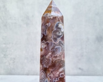 May include: A brown and white agate crystal point with a pointed tip and a smooth, polished surface. The crystal has a unique pattern of swirling colors and textures.
