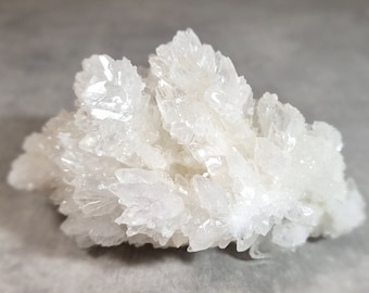 Op de afbeelding: Een cluster van doorschijnende witte kristallijne mineraalformaties met scherpe, puntige randen. Het exemplaar bevat talloze kleine, grillige punten die vanuit een centrale basis naar buiten stralen, wat een complexe en reflecterende oppervlakte creëert.