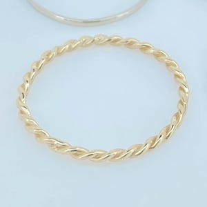 May include: Six rings in gold and silver are shown against a white backdrop. Two gold and two silver rings have a plain band. The other two rings have a twisted rope design, one gold and one silver.