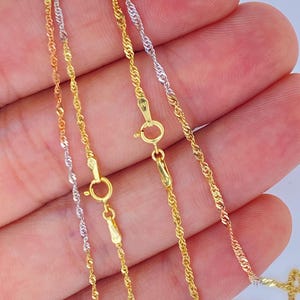 May include: Close-up of three delicate gold necklaces in yellow, white, and rose gold. Each chain features a twisted rope design and a secure clasp. The necklaces are displayed against a neutral background.