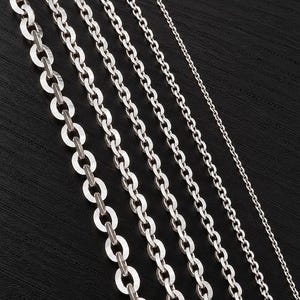 May include: Five silver-toned metal chains arranged in parallel, ranging from a thick, wide oval link chain on the left to a very thin, delicate round link chain on the far right. Each chain features a polished, reflective metallic finish.