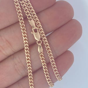 Pu&ograve; includere: Una collana a catena a maglia curb color oro con chiusura a moschettone. La catena &egrave; composta da piccole maglie ad incastro. La collana &egrave; esposta su uno sfondo chiaro.
