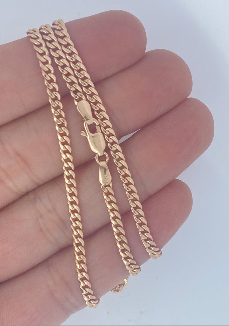 Pu&ograve; includere: Una collana a catena a maglia curb color oro con chiusura a moschettone. La catena &egrave; composta da piccole maglie ad incastro. La collana &egrave; esposta su uno sfondo chiaro.