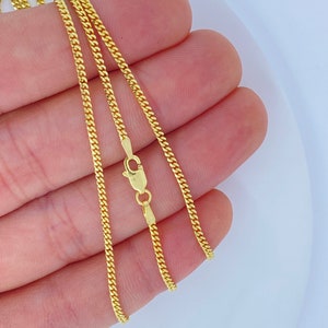 May include: A gold chain necklace with a curb link style. The chain is shown on a hand, with the clasp visible.