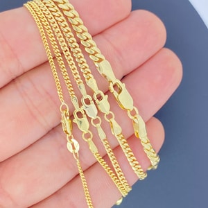 May include: Five gold chains of different widths and lengths, displayed on a hand.