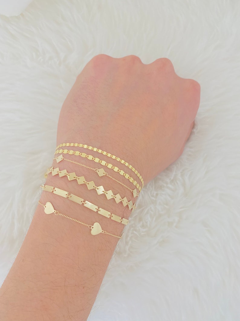 K&ouml;nnte beinhalten: Ein Set aus f&uuml;nf goldenen Armb&auml;ndern mit verschiedenen Kettenarten. Die Armb&auml;nder haben Herz-, Quadrat- und Rechteckglieder.