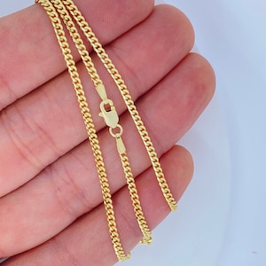 May include: A gold curb chain necklace with a lobster clasp. The chain is shown folded in a hand.
