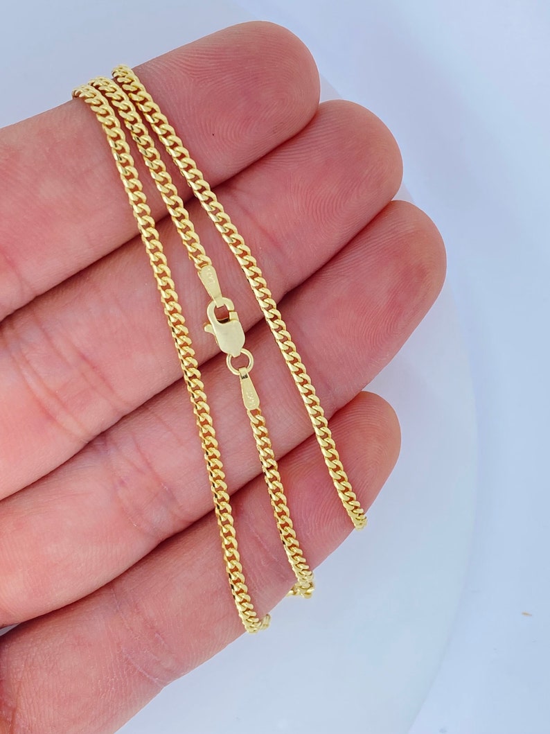 May include: A gold curb chain necklace with a lobster clasp. The chain is shown folded in a hand.