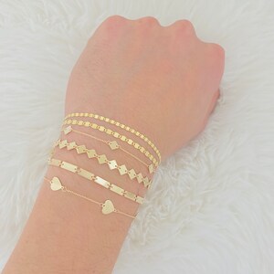 K&ouml;nnte beinhalten: Ein Set aus f&uuml;nf goldenen Armb&auml;ndern mit verschiedenen Kettenstilen. Die Armb&auml;nder umfassen eine herzf&ouml;rmige Kette, eine Stabkette, eine quadratische Kette und zwei ovale Ketten.