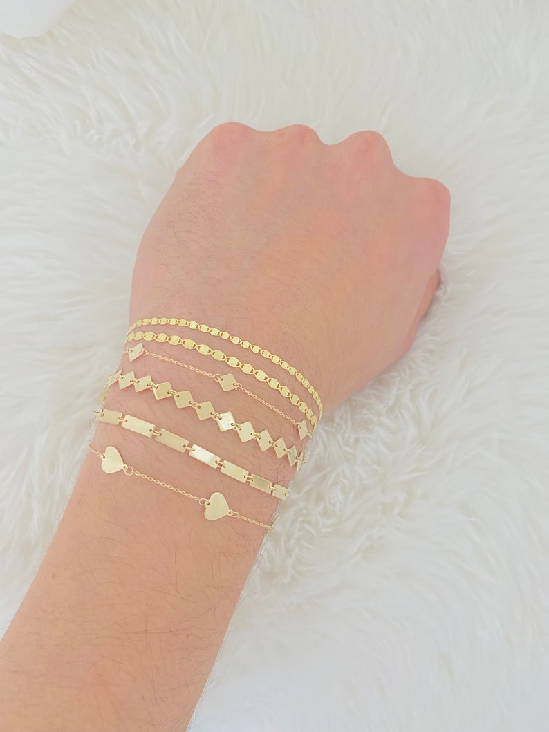 K&ouml;nnte beinhalten: Ein Set aus f&uuml;nf goldenen Armb&auml;ndern mit verschiedenen Kettenstilen. Die Armb&auml;nder umfassen eine herzf&ouml;rmige Kette, eine Stabkette, eine quadratische Kette und zwei ovale Ketten.