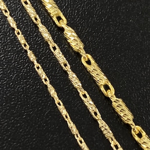 Puede incluir: Primer plano de tres collares dorados con diferentes diseños de cadena. Las cadenas tienen eslabones texturizados y se muestran sobre un fondo oscuro. Los collares varían en grosor y estilo de eslabones.