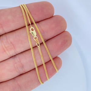 May include: A gold chain necklace with a lobster clasp. The chain is a delicate, thin, and flat curb style.