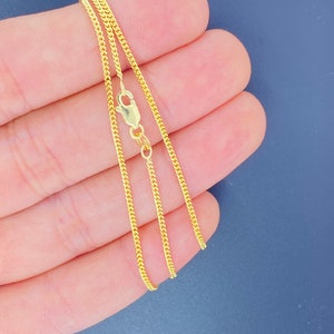 May include: A gold chain necklace with a lobster clasp. The chain is a delicate, thin, and flat curb style.