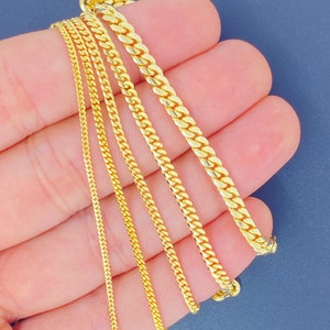 May include: Five gold chains of different widths and lengths, displayed on a hand.