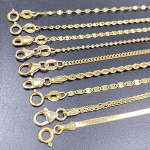 May include: A collection of gold necklaces with various chain styles, including beaded, rope, and flat designs. Each necklace features a clasp for secure wear. The chains are displayed against a dark background.