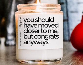 Może przedstawiać: Zapalone świeca w szklanym słoiku z białą etykietą. Na etykiecie napisano "you should have moved closer to me, but congrats anyways." Słoik ma 255 g i czas palenia 45 godzin.