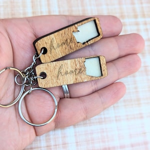 May include: Two wooden keychains with the state of Washington cut out and the word "home" engraved on each. The keychains are attached to a silver key ring.