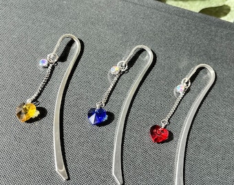 May include: Three silver bookmark pendants with dangling crystal hearts. The hearts are red, blue, and yellow.
