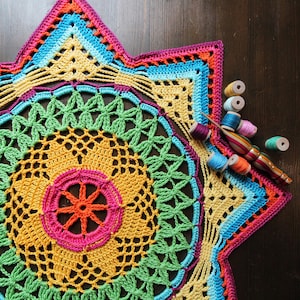 Könnte beinhalten: Ein farbenfroher Häkel-Sternenstrahl mit einem mehrfarbigen Zentrum und einer Vielzahl von Garnfarben im Hintergrund.