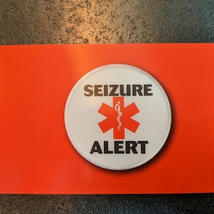 Könnte beinhalten: Rote Plastikkarte mit einem weißen Kreis, der einen roten Stern des Lebens mit einem Schlangen- und Stabsymbol und dem Text "SEIZURE ALERT" enthält.