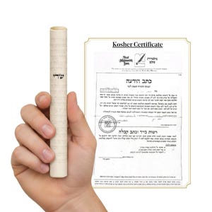 Puede incluir: Un pergamino enrollado con texto hebreo se sostiene junto a un certificado Kosher. El certificado tiene texto en hebreo e inglés, con un borde dorado. El pergamino es de color blanquecino con texto hebreo.