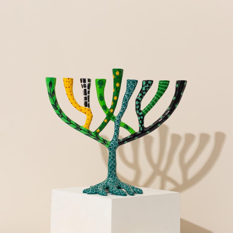 May include: A green, yellow, and black menorah with a tree-like design. The menorah has a unique, hand-painted design with swirls, leaves, and dots.